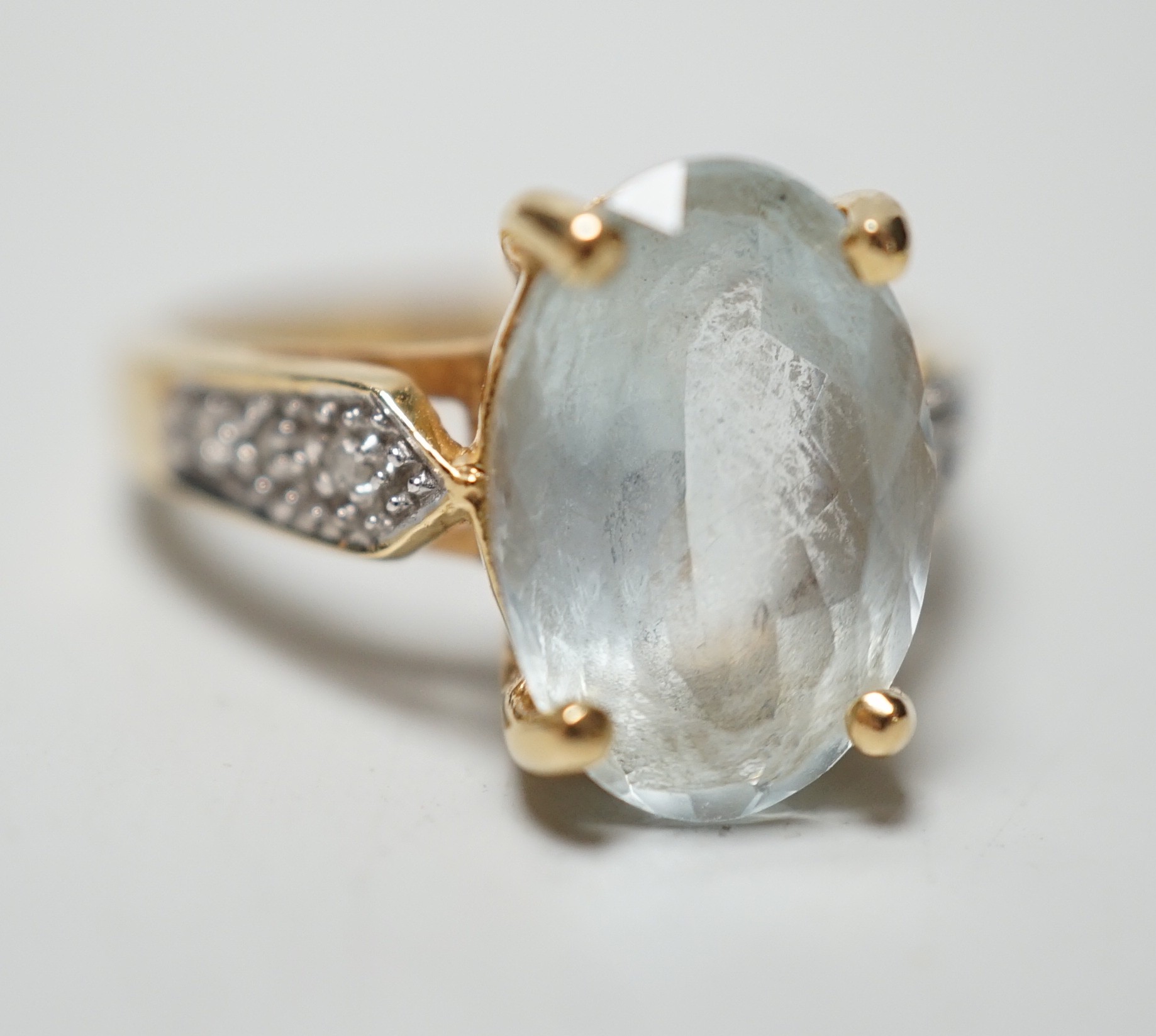 A modern 18ct gold and oval cut aquamarine set dress ring, with diamond chip set shoulders, size N, gross weight 5.5 grams.